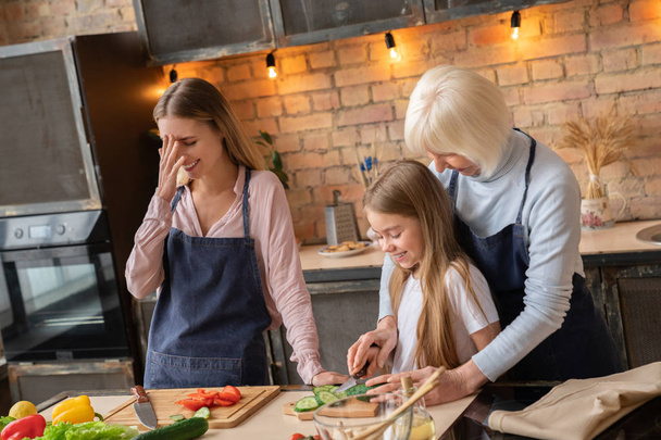 Little girl with her mother and grandmother having fun while cooking in kitchen - Valokuva, kuva