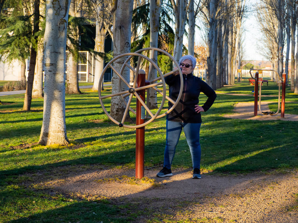 A senior woman with white hair practicing gymnastics in a bio-healthy park - Foto, Imagen