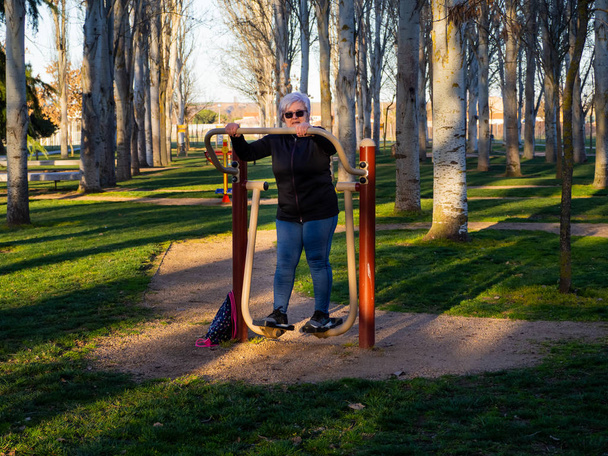 Старшая женщина с седыми волосами, практикующая гимнастику в биоздоровом парке
 - Фото, изображение