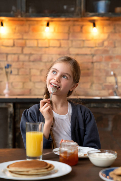 Happy little child taste jam on the spoon during the breakfast in kitchen with light bulb on the background - 写真・画像