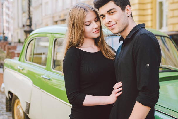 Young multiracial couple, male and female lovers heterosexual people students. Beautiful models posing standing near a retro car in the city. Dressed in black clothes - Photo, Image