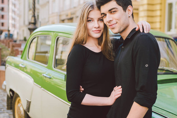 Young multiracial couple, male and female lovers heterosexual people students. Beautiful models posing standing near a retro car in the city. Dressed in black clothes - Photo, Image