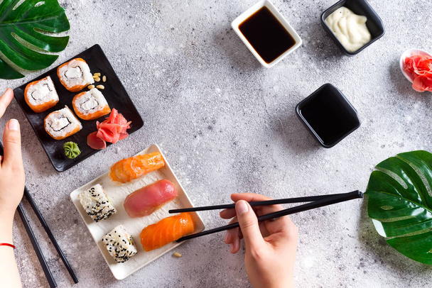 Varios sushi fresco y delicioso conjunto en pizarra blanca y negra con palos de metal y pizarra, salsa y mano sobre fondo de piedra clara, plano laico
 - Foto, Imagen