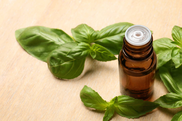 Bottle of basil essential oil and fresh leaves on wooden table. Space for text - Foto, imagen