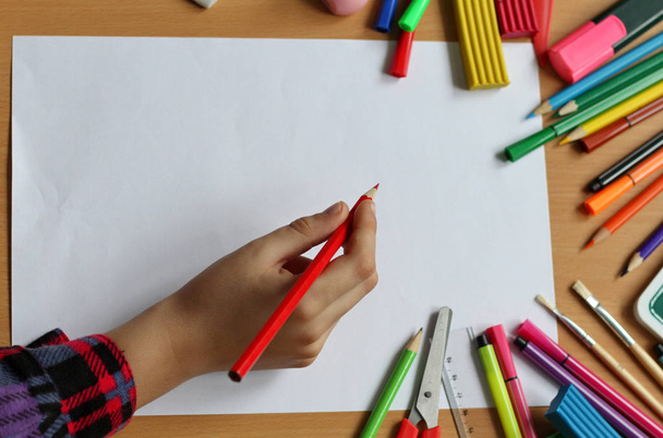 白紙の紙と赤ちゃんの手の鉛筆を持つテーブルの上のビュー。学校に戻るペイントブラシ、鉛筆、プラネインでカラーペイント。キッズペインティングコンセプト。子供のアート. - 写真・画像