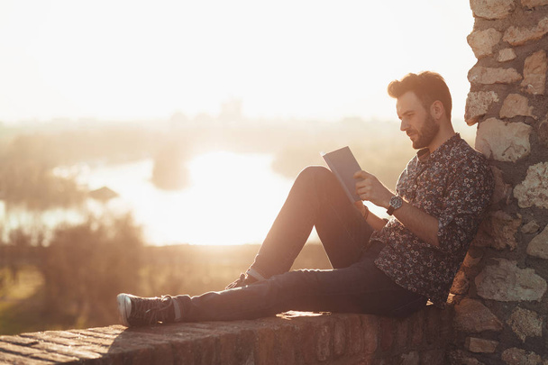 Jeune homme lisant un livre en plein air au coucher du soleil
 - Photo, image