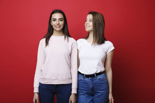 Δύο νεαρές όμορφες φιλενάδες απομονωμένοι σε ένα κόκκινο φόντο, ενώ  - Φωτογραφία, εικόνα