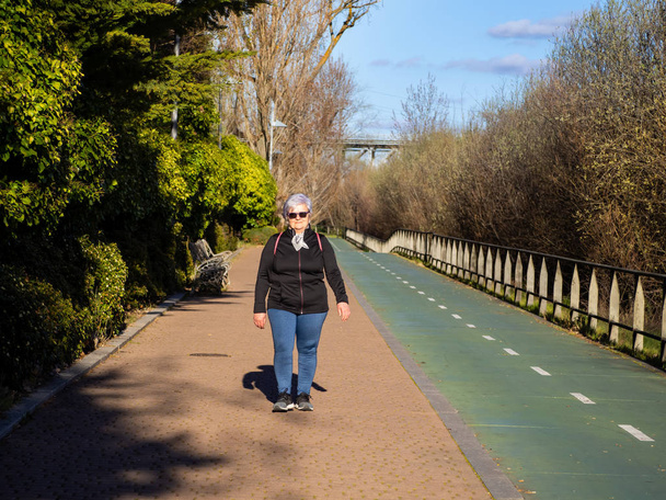 Starsza kobieta z białym włosami słuchanie chodzenia w parku miejskim - Zdjęcie, obraz