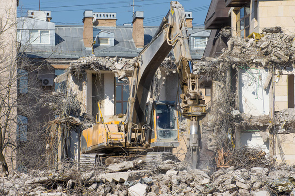 Escavatore con cesoie idrauliche sullo sfondo di un edificio demolito. Smontaggio della costruzione di emergenza
. - Foto, immagini
