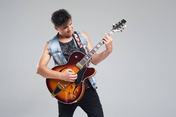 Young man musician with an electric guitar in hand on a gray background. he plays rock and roll loudly.  - Foto, afbeelding