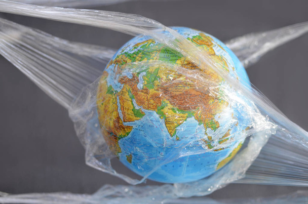 The earth is suspended in a plastic plastic disposable packaging, on a dark background. The concept of environmental pollution by polyethylene plastic waste, environmental problems. - Foto, Bild