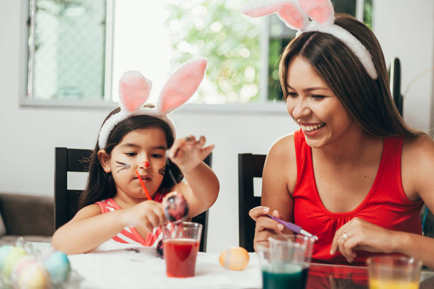 Happy easter! A mother and her daughter painting Easter eggs. Happy family preparing for Easter. Cute little child girl wearing bunny ears on Easter day - Photo, image