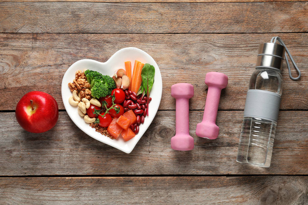 Flat lay composition with plate of products for heart-healthy diet on wooden background - Foto, afbeelding
