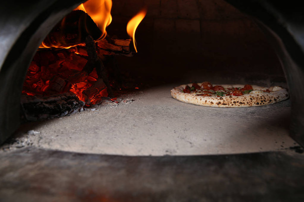 Burning firewood and tasty pizza in oven at restaurant kitchen - Фото, изображение