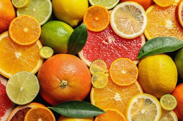 Sliced and whole citrus fruits with leaves as background, top view - Zdjęcie, obraz