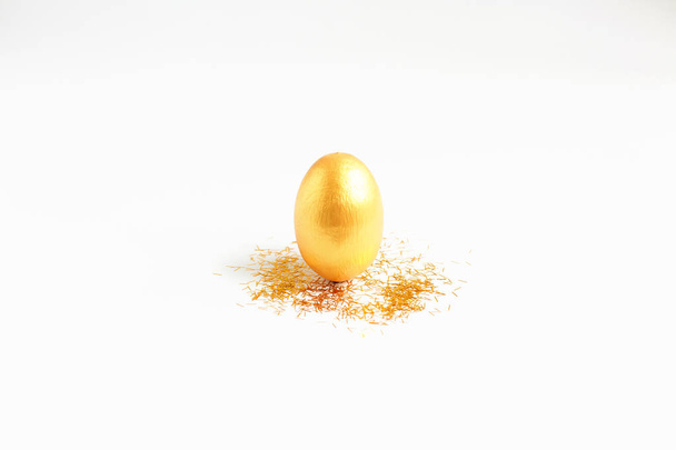 Huevo de oro, un símbolo de hacer dinero y la inversión exitosa, de pie sobre fondo blanco. Concepto de Semana Santa Mínima Feliz. flatlay
. - Foto, Imagen