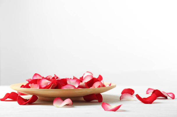 Деревянная тарелка с лепестками роз на столе на белом фоне. Пространство для текста
 - Фото, изображение