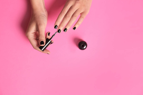 Woman applying nail polish on color background, top view with space for text - Foto, imagen