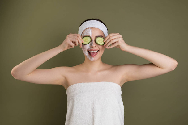 Веселая красивая женщина, завернутая в полотенце, закрывая глаза огуречными ломтиками
 - Фото, изображение