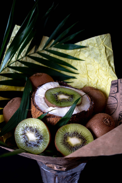 Bouquet festif unique de brindilles de noix de coco, kiwis et palmiers sur fond noir. Bouquet de fruits. Fruits et légumes du concept de santé
. - Photo, image