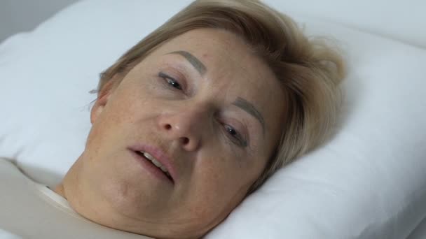 Disappointed aged woman lying in bed, closing face with trembling hand, crisis - Imágenes, Vídeo