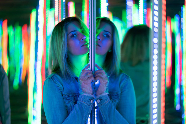 dulce chica caucásica camina en un laberinto de espejos con diodos de colores y disfruta de una inusual sala de atracción en la ciudad
 - Foto, imagen