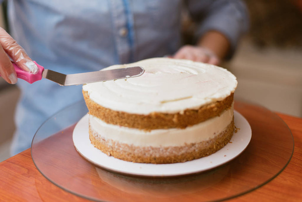 El confitero niveló la crema en el pastel. El cocinero crea un pastel, lo recoge y lo cubre con crema y luego lo nivela con una espátula y un raspador
. - Foto, Imagen