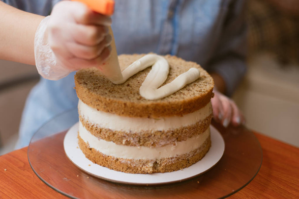 ζαχαροπλάστης σφίγγει η κρέμα στην τούρτα. Κορίτσι κάνει ένα κέικ - Φωτογραφία, εικόνα