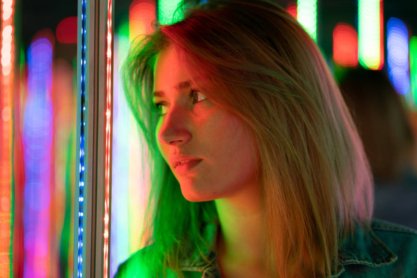 sweet caucasian girl walks in a mirror maze with colorful diodes and enjoys an unusual attraction room in the city - Photo, image