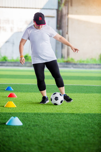 Жінка-футболістка біжить і контролює футбольний м'яч між конусом
 - Фото, зображення