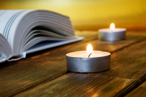 Un livre ouvert de contenu religieux se trouve sur des planches de bois sur un fond doré. A proximité se trouvent des bougies allumées
.  - Photo, image
