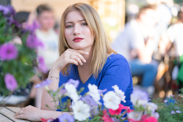 Чарівна біла дівчина в блакитній сукні сидить за столом у міському кафе і чекає на самоті влітку
 - Фото, зображення