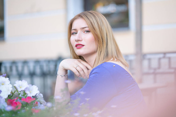 uroczy kaukaski blond dziewczyna w niebieskiej sukience, siedząc przy stoliku w kawiarni city sam i czeka - Zdjęcie, obraz