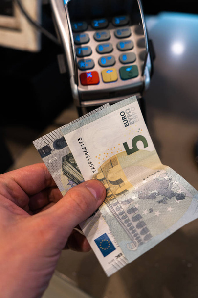 Mano de hombre sosteniendo billetes de euro cerca de una terminal de pago POS en una cafetería
 - Foto, Imagen
