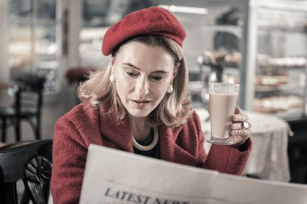 Attentive blonde female reading newspaper in cafe - Photo, Image