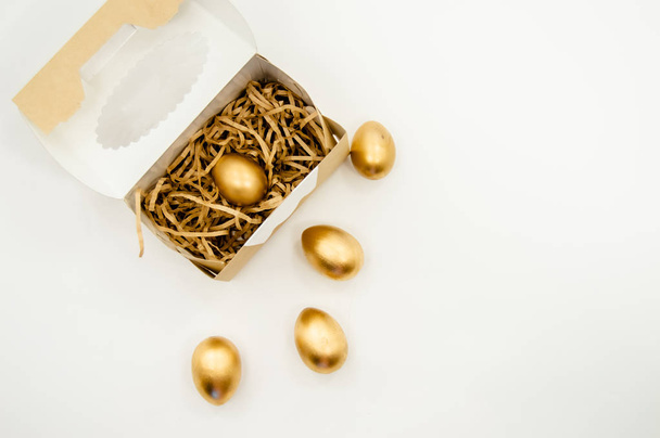 Χρυσά Πασχαλινά αυγά σε ένα κουτί με χρυσά αστέρια σε λευκό φόντο. Διακοπές το Πάσχα έννοια αφηρημένη φόντο copyspace κάτοψη  - Φωτογραφία, εικόνα