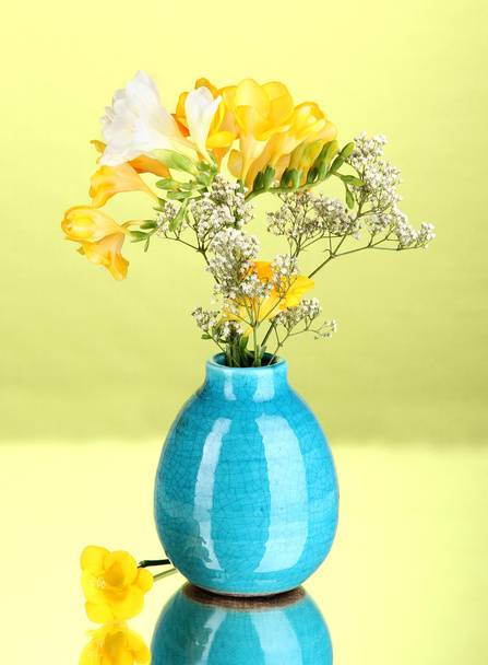 Beautiful bouquet of freesia in vase on green background - 写真・画像