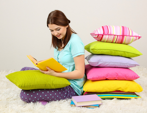 Beautiful young girl with pillows and books in room - Foto, Imagem