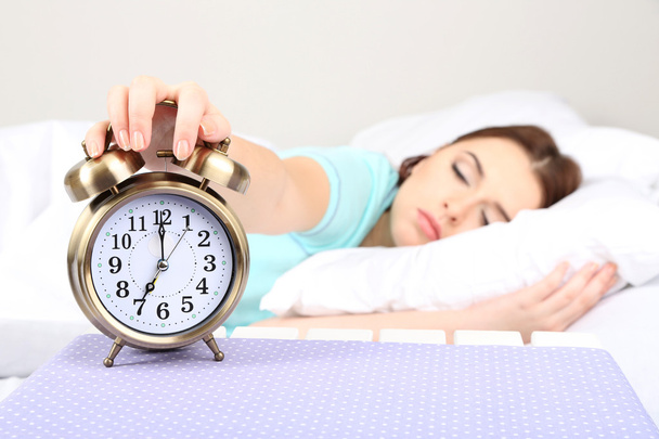 Beautiful young woman sleeping on bed with alarm clock in bedroom - Foto, Bild
