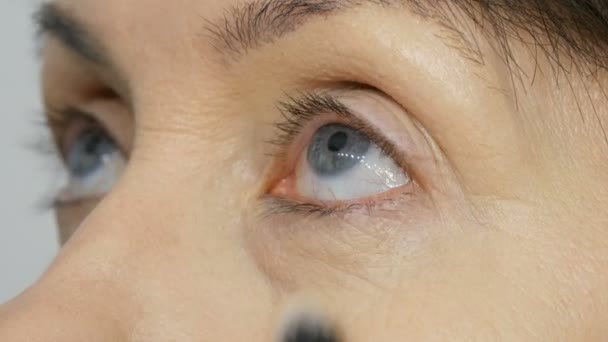 Make-up Artist doen make-up met markeerstift concealer aan middelbare leeftijd vrouw met blauwe ogen. Leeftijd make-up. Close-up portret. Breng poeder met penseel - Video
