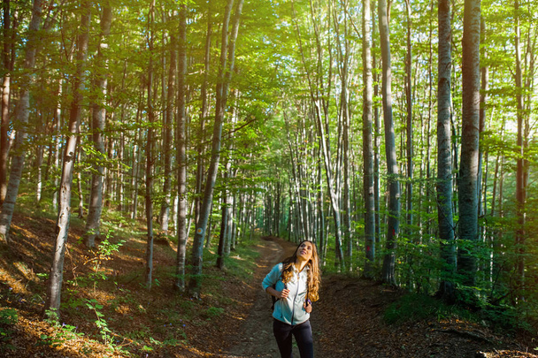 Молода жінка прогулюється в лісі, несучи рюкзак в лісі на заході сонця світло в осінній сезон
. - Фото, зображення
