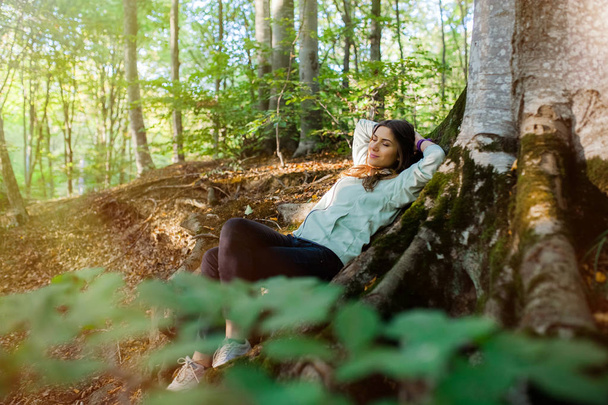 Молода жінка прогулюється в лісі, несучи рюкзак в лісі на заході сонця світло в осінній сезон
. - Фото, зображення