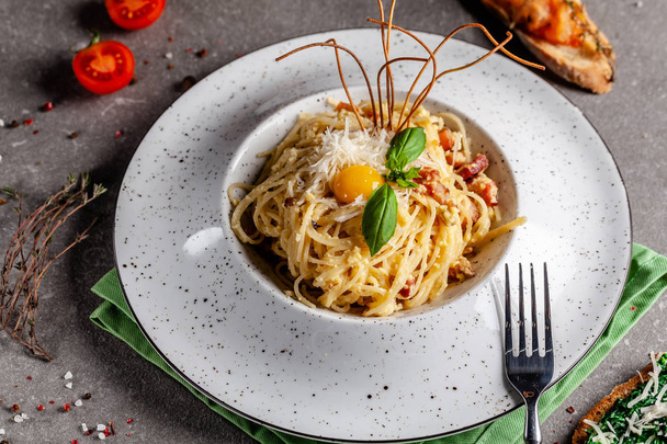 The concept of Italian cuisine. Pasta carbonara with bacon, parmesan and egg yolk. The decor of fried spaghetti. Serving dishes in a restaurant in a white plate. copy space - Fotó, kép