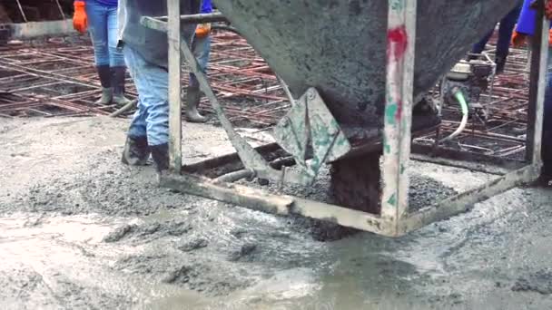 Hombre trabajador que utiliza una cesta de acero de hormigón para el cemento después de verter hormigón premezclado en el refuerzo de acero para hacer la carretera mediante la mezcla móvil de la hormigonera
. - Metraje, vídeo