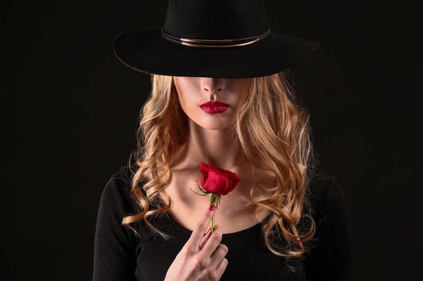 schöne junge Frau mit Blume auf dunklem Hintergrund - Foto, Bild