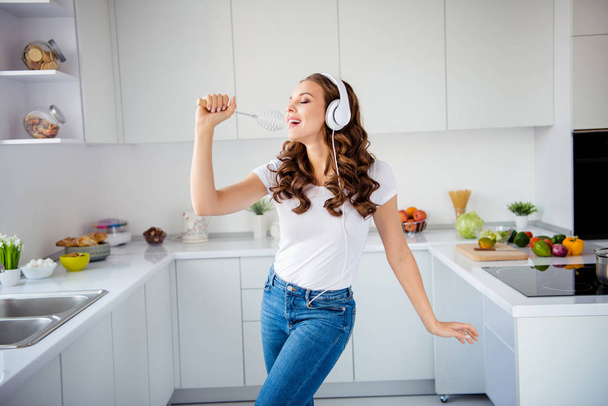 Portrait of her she nice-looking attractive lovely charming cheerful cheery wavy-haired girl holding in hand kitchenware like mic in modern light white interior style room - Fotografie, Obrázek