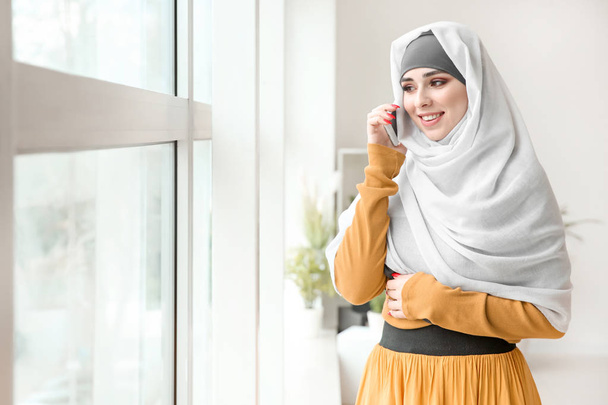 Beautiful Muslim woman talking by phone near window - Foto, imagen