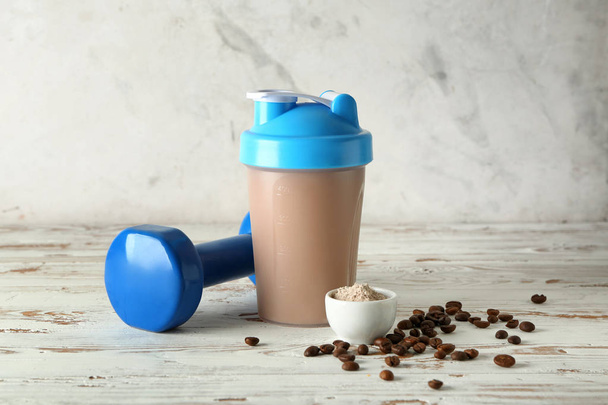 Bottle of protein shake with dumbbell on white wooden table - Photo, Image