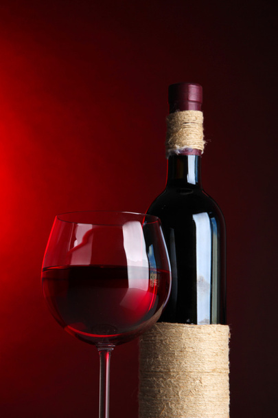 Copa de vino con botella sobre fondo rojo brillante
 - Foto, imagen
