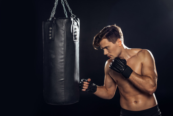 Beau boxeur dans l'entraînement des gants de boxe avec sac de boxe sur noir
 - Photo, image